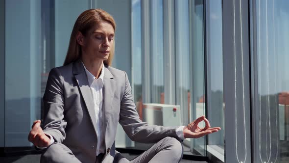 Calm Tired Business Woman Dressed in Classic Suit Meditate in Lotus Position alt