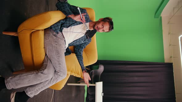 Caucasian Male Video Blogger Sits on a Yellow Chair in the Studio Talking