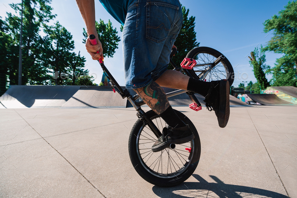 Cropped picture of an unrecognizable mature tattooed man balancing on his bmx in a skate park.