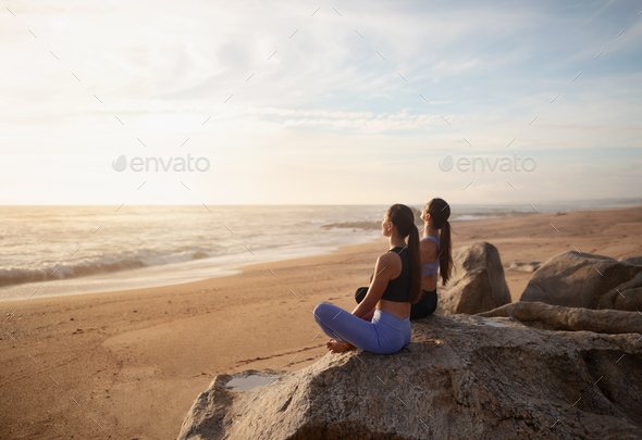 Calm happy young european women twins in sportswear practice yoga on sea  beach, enjoy morning peace Stock Photo by Prostock-studio