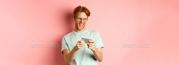 Happy young man with red messy haircut wearing glasses playing  