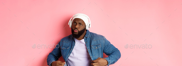 Cool and sassy Black guy dancing, listening to music in headphones, looking confident, standing