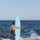 Back view of young surfer standing barefooted on sandy shore, - PhotoDune Item for Sale