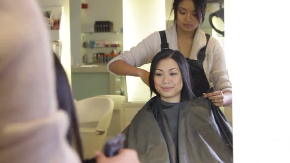 WS, Female client sitting in hairsalon, Hairstylist putting on cape alt