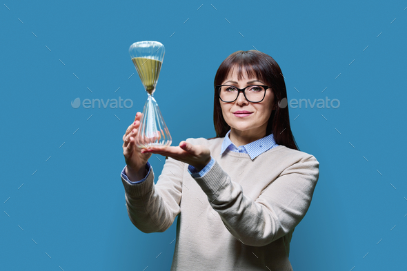 Mature woman holding an hourglass in her hands, on gray background