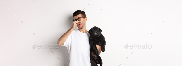 Dog owner squinting and shutting nose from disgusting reek, holding pug with bed smell, standing