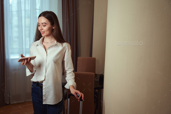 Lady looking at phone in hotel room with window behind