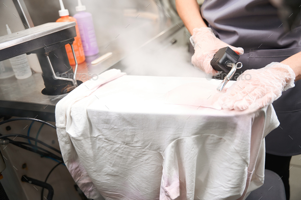 Worker of dry-cleaning service doing pre treatment, using steam gun ...