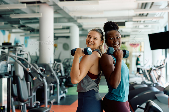 Happy athletic women using hand weights while exercising in a gym.