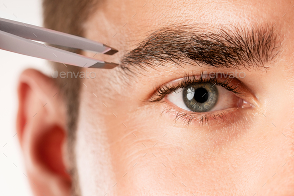 Male eye and tweezers for eyebrow grooming and shape correction