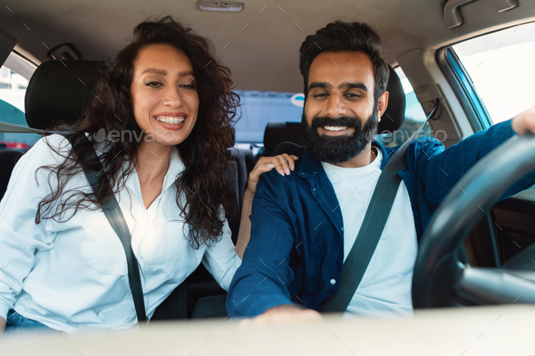 Excited arab couple enjoying car ride sitting in new automobile inside, spouses driving and testing