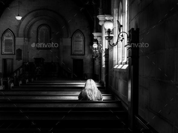 Grayscale rear view shot of a female praying in an empty church