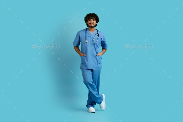 Smiling young handsome indian man doctor posing on blue