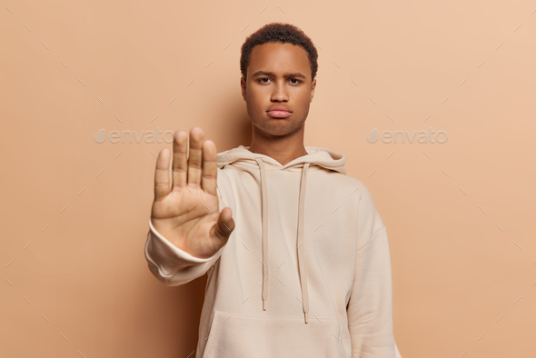 Stop gesture. Strict displeased young African man raises hand dressed in casual sweatshirt asks not