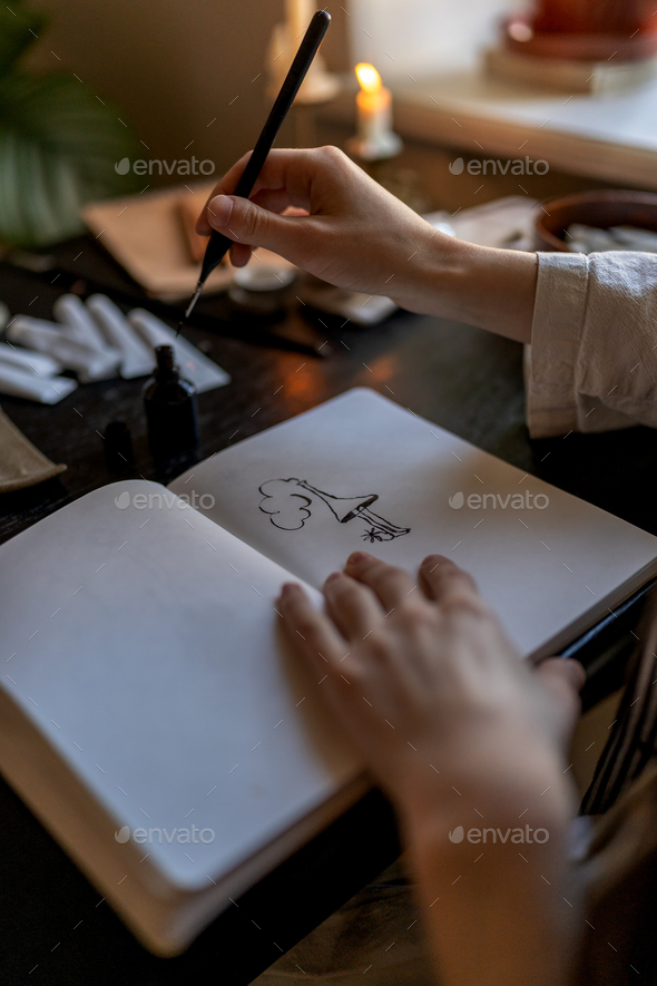Creative work, passion, hobby. Artist sitting table with burning candles drawing ink in notebook.