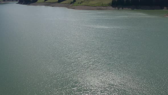 Drone flying over blue lake, tilting up to typical Swiss landscape alt