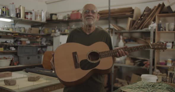 Old man holding a guitar in a wood workshop