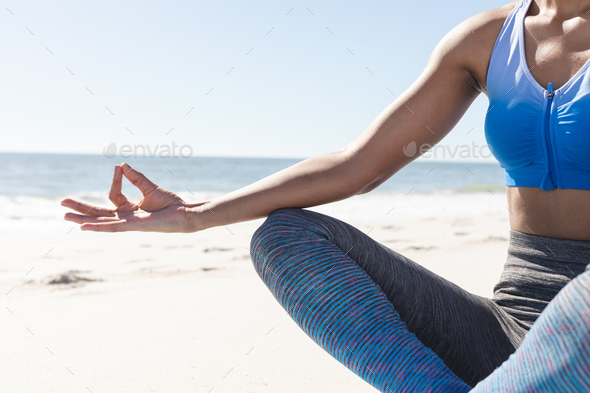 Midsection of fit african american woman practicing yoga meditation sitting  on sunny beach Stock Photo by Wavebreakmedia