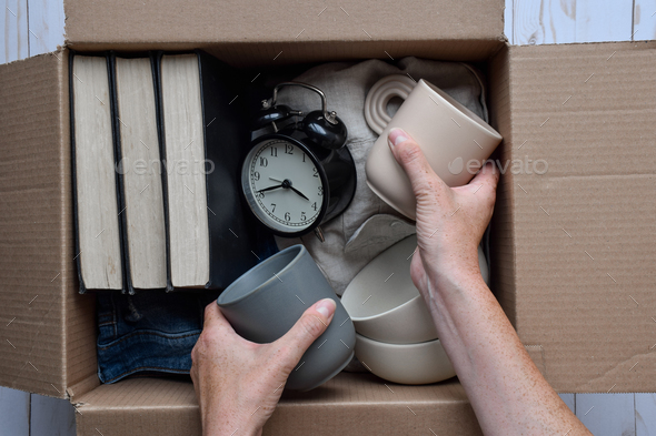 Person\'s hands placing used personal belongings items into cardboard box