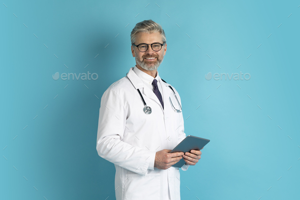 Cheerful mature doctor using digital tablet on blue background