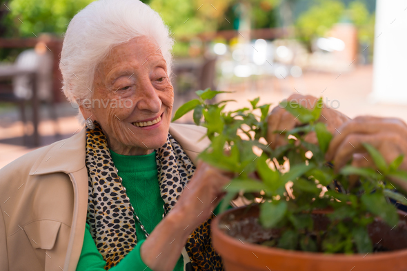 An elderly woman taking care of the flowers in the garden of a nursing home or retirement home