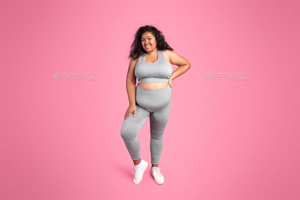 Full length shot of happy black overweight lady in sportswear posing and smiling at camera isolated