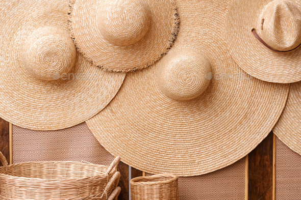 Group of straw floppy hats hanging on woven partition with wicker baskets for sale in street market