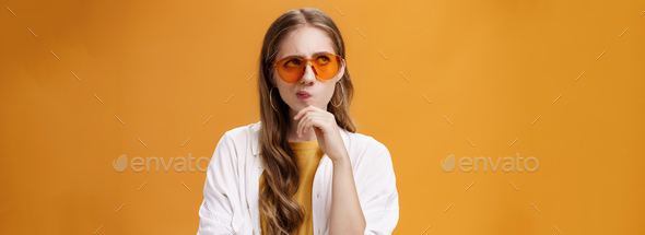 Thoughtful stylish party girl with long wavy natural hairstyle in trendy sunglasses and blouse