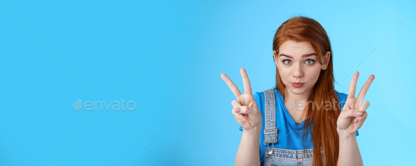 Playful cute silly redhead girlfriend making funny face, show peace victory signs, hold breath