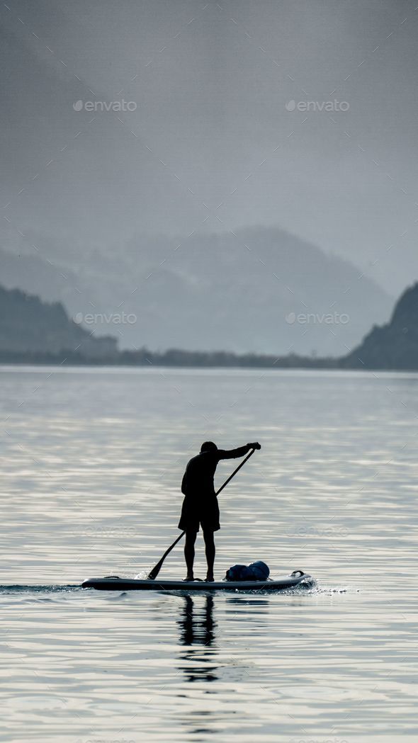 Adult male paddling a surfboard on a large body of water with a scenic ...