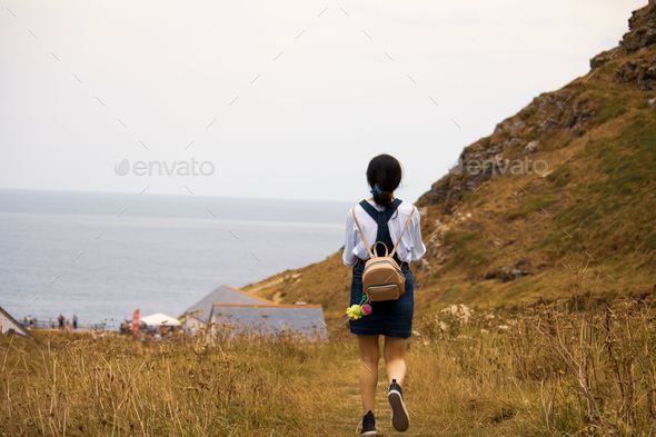 Female student is walking up a hill with a backpack strapped to her.