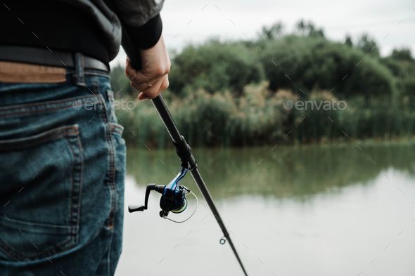 a man with a fishing rod in his hand is looking back at the water Stock  Photo by wirestock