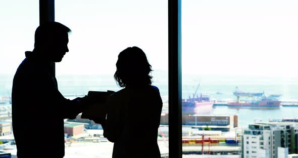 Silhouette of male and female executives discussing over digital tablet alt