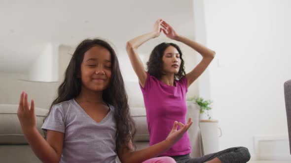 Hispanic mother and daughter sitting on the floor meditating at home alt