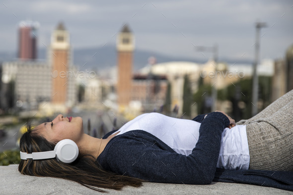 Relaxed young woman lying in balcony while listening music with headphones. Confident young lady