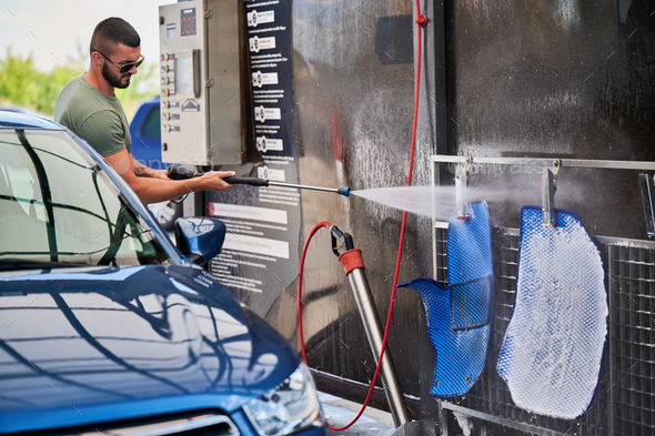 Confident man washing car mats on self-service car-washing station.