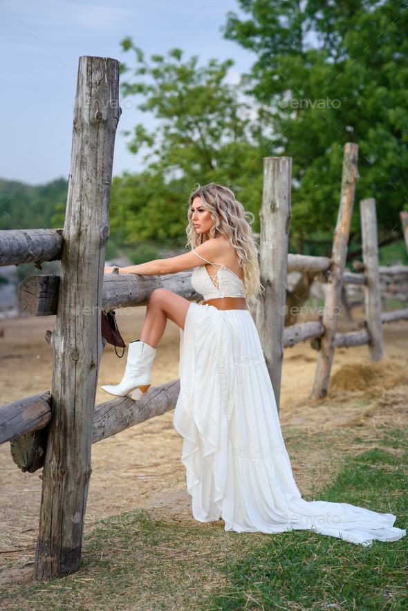 beautiful cowgirl style model posing on farmland. A beautiful girl in a white dress, a cowboy hat po