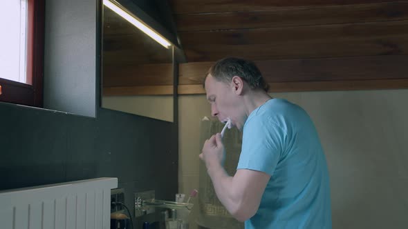 Man Brushing Teeth in the Morning While Standing in the Bathroom alt