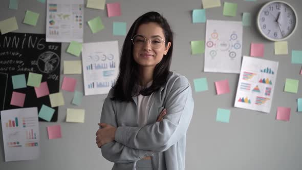 Happy young hipster teen girl wearing glasses looking at camera and posing indoors in modern office alt