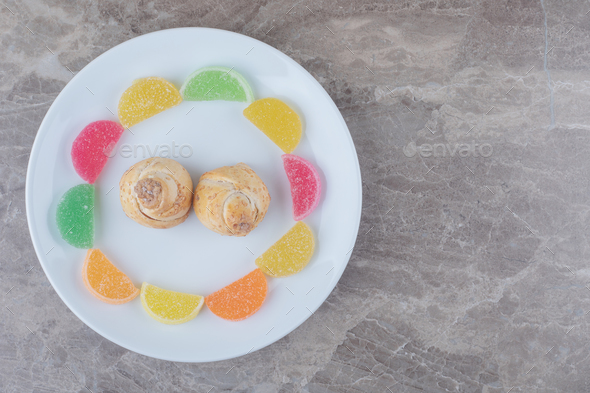 Marmelades around tiny cakes on a platter on marble background