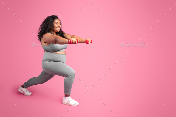Black chubby woman holding dumbbells and making lunges exercise, training  legs over pink studio Stock Photo by Prostock-studio