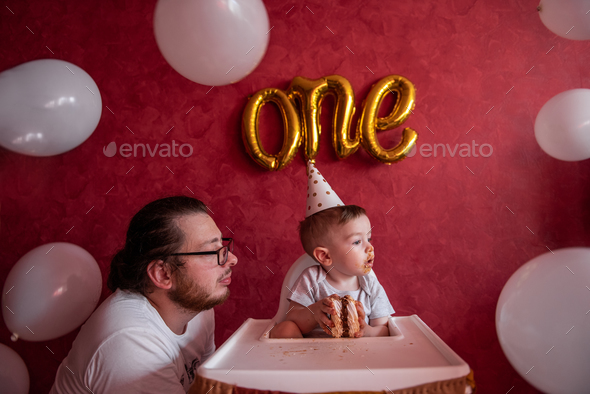 Father celebrates with little son his first birthday. Man fooling around with boy, eats holiday cake
