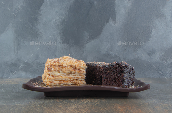 Slices of napoleon and chocolate cakes on a platter on wooden background