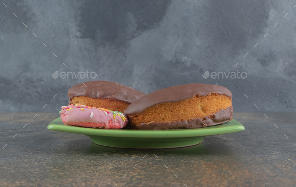 A donut and chocolate coated cakes on a platter on wooden background