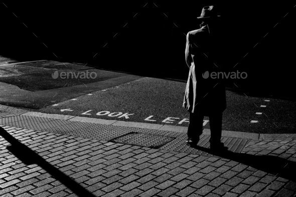 Man standing in a lonely street at night, shadows falling on street