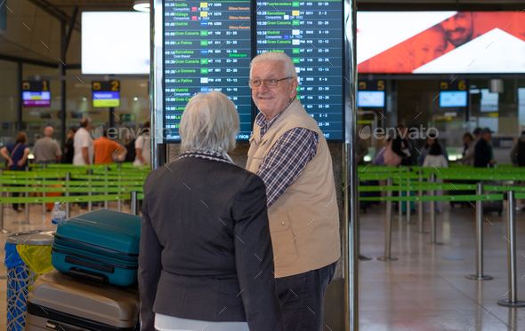 Back view of white haired senior couple pushing luggage trolley walking in the airport area