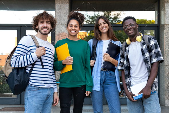 Happy multiracial college students standing in front of university ...