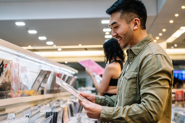 Happy ethnic man choosing vinyl record in shopping center