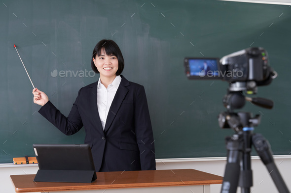 A Japanese female teacher filming an online class in her classroom - Stock Photo - Images