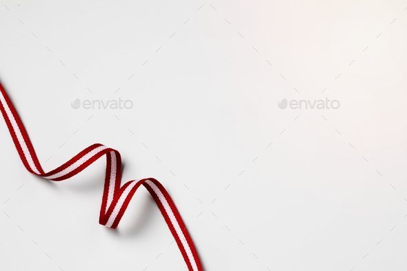Thin, red and white ribbon is laid out on a plain white background Stock  Photo by wirestock
